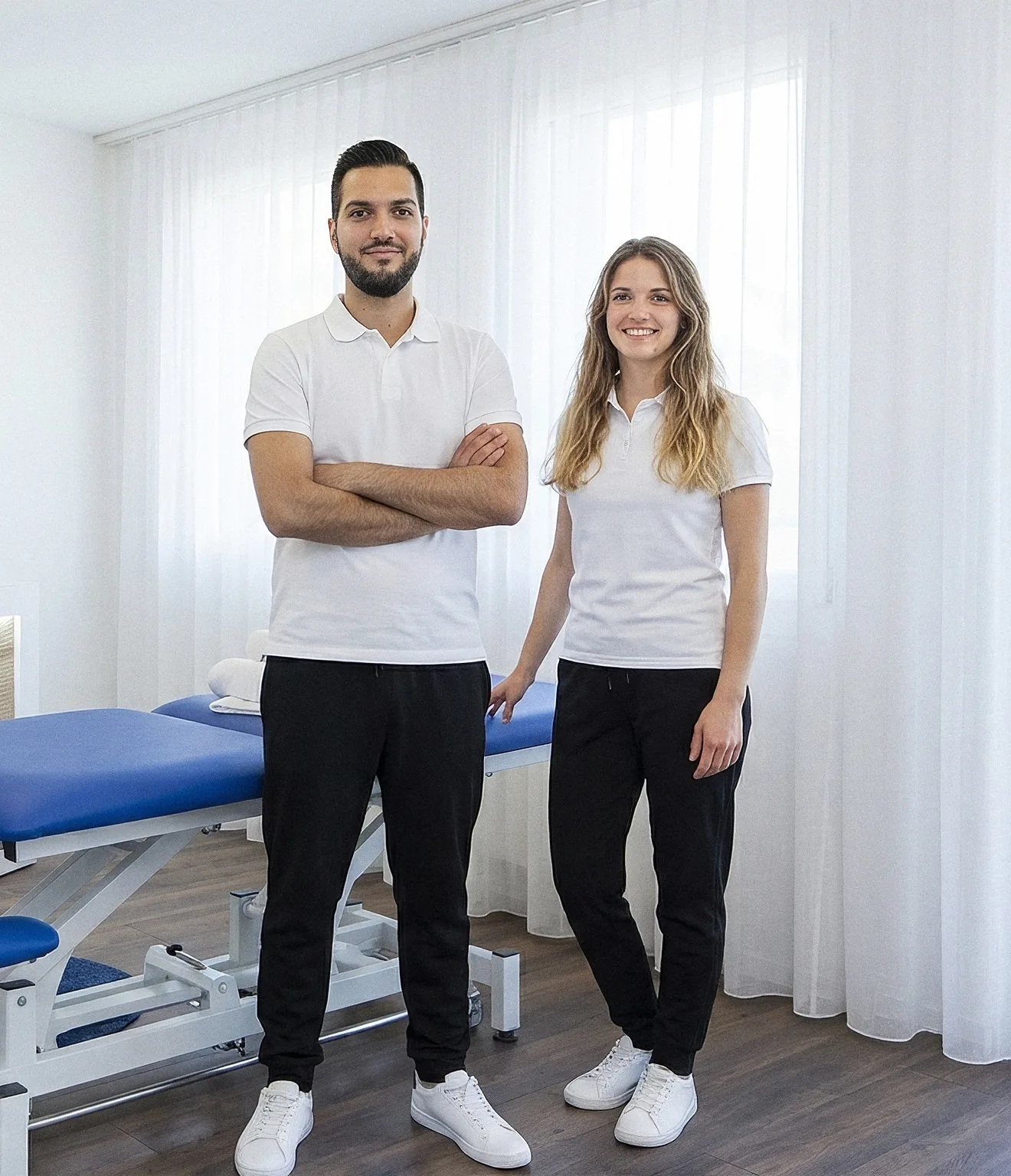 Murat Aydin und Dominique Wüthrich in weissen Poloshirts stehen neben der Behandlungsliege im Behandlungsraum der MassagePraxis Aydin in Cham